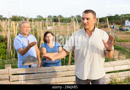 Homme en train de se quereller avec des voisins de couple mûrs dans le jardin de l'arrière-cour Banque D'Images