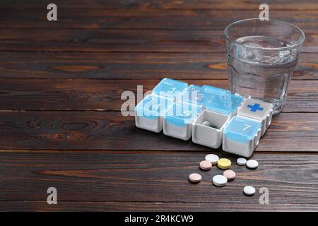 Boîte de pilules avec des médicaments et un verre d'eau sur une table en bois. Espace pour le texte Banque D'Images