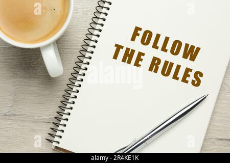 Carnet avec phrase Suivez les règles, stylo et tasse de café sur table en bois, plat Banque D'Images