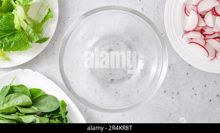 Salade de printemps dans un bol en verre. La laitue romaine, les jeunes épinards et les tranches de radis frais sont en gros plan sur la table de cuisine, à plat avec espace pour les copies Banque D'Images