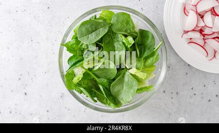 Salade de printemps dans un bol en verre. La laitue romaine, les jeunes épinards et les tranches de radis frais sont en gros plan sur la table de cuisine, à plat avec espace pour les copies Banque D'Images