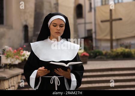 Jeune nun lisant la Bible près de bâtiment à l'extérieur. Espace pour le texte Banque D'Images