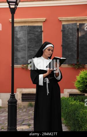 Jeune nun lisant la Bible près de bâtiment à l'extérieur Banque D'Images
