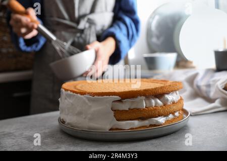 Femme décorant délicieux gâteau de couche maison avec de la crème à table grise, gros plan Banque D'Images