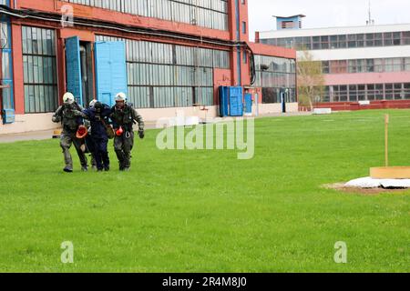 Trois sauveteurs de pompiers en combinaisons de protection ignifuges et casques emmenez la personne blessée dans un masque à gaz de la zone de danger Banque D'Images