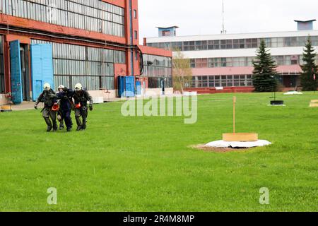 Trois pompiers du secouriste en combinaisons et casques de protection ignifuges emmenez la personne blessée dans un masque à gaz de la zone de danger de l'usine Banque D'Images