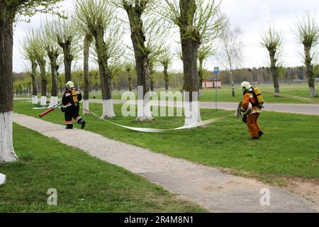 Les pompiers professionnels, les sauveteurs en combinaisons de protection ignifuges, les casques et les masques à gaz fuient les gens avec un tuyau d'incendie, un tuyau d'eau. Banque D'Images