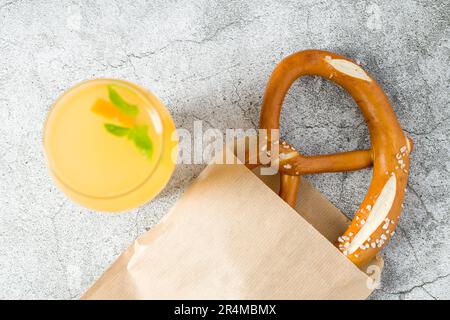 Bretzel enveloppé dans du papier d'emballage avec une boisson à côté sur une table en pierre Banque D'Images