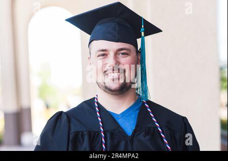 Portrait souriant d'un homme diplômé en casquette et robe noires Banque D'Images