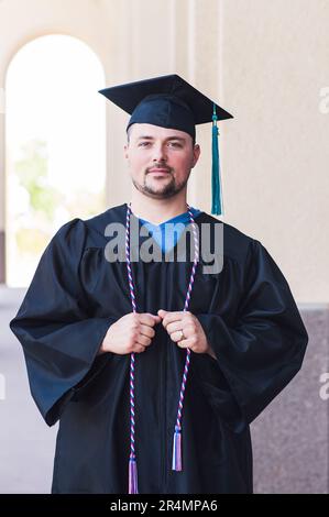 Portrait souriant d'un homme diplômé en casquette et robe noires Banque D'Images