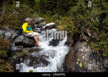 Full length view of women cooling tired feet in a cold alpine river. Banque D'Images