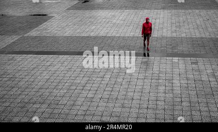 Un homme au manteau rouge traverse une place pavée sous la pluie à Danang, au Vietnam Banque D'Images