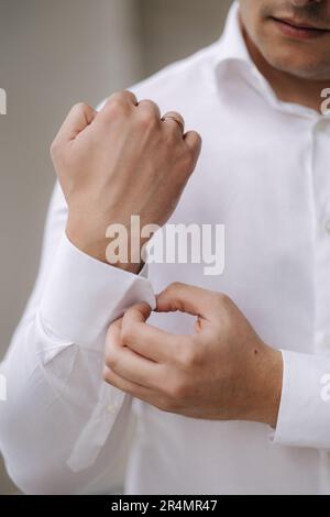 Photo de l'homme fixe le lien de manchette sur la manche de chemise. Se lève le matin lors du mariage. Gros plan Banque D'Images