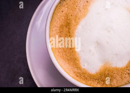 Gros plan, gros plan sur un café Cappuccino chaud avec une tasse blanche sur une table en bois noir, vue du dessus Banque D'Images