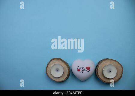 Coeur avec je vous aime entre les bougies placées dans des rondins ronds, photographiés d'en haut, placé sur le bord d'un fond bleu. Banque D'Images