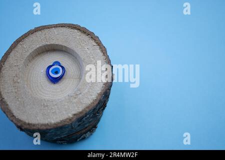 La petite bûche et la perle de l'œil maléfique à l'intérieur, photographiée d'en haut, placée sur le bord du fond bleu. Banque D'Images