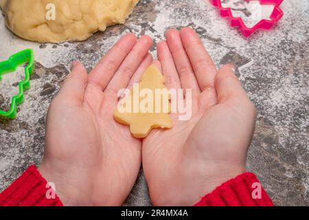 La main avec les enfants sous forme de cookies de Noël pour les enfants, making gingerbread dans la forme de l'homme. Nouvelle année traiter pour le Père Noël la cuisson. Pâte crue. Des Banque D'Images