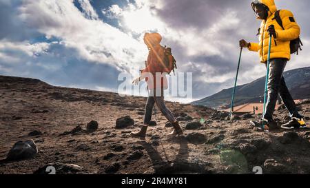 Couple de randonneurs en équipement technique marchant sur un sentier de roche de lave à l'Etna. Elles sont rétroéclairées contre un ciel très nuageux. Banque D'Images