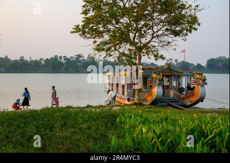 Un bateau-dragon amarré sur la rivière des parfums et une famille locale se rendant sur la vie quotidienne sur la rive de Hue, au Vietnam. Banque D'Images