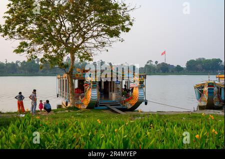 Un bateau-dragon amarré sur la rivière des parfums et une famille locale se rendant sur la vie quotidienne sur la rive de Hue, au Vietnam. Banque D'Images