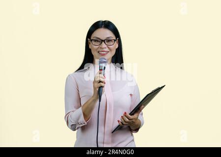 La femme d'affaires donne un discours dans le microphone. Isolé sur jaune pastel. Banque D'Images