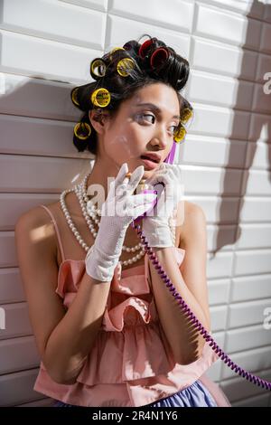 brunette et la jeune femme asiatique avec des pillards en haut à volants roses, collier de perles et gants blancs, fumer la cigarette et parler rétro Banque D'Images