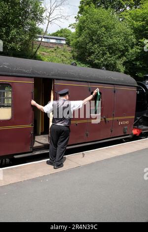 Un garde sur le chemin de fer Keighley & Worth Valley Heritage signale immédiatement le passage par un drapeau vert avant d'embarquer dans le train Banque D'Images