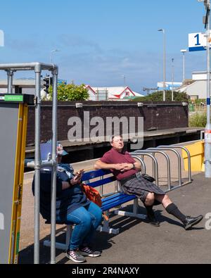 25 mai 2023. Gare de Mallaig, Mallaig, Écosse. C'est un homme habillé dans le four à tartan ayant un peu de sommeil en étant assis sur un banc. Banque D'Images