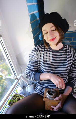 une jeune femme heureuse moud le café avec un vieux moulin fait à la main dans la cuisine, souriant Banque D'Images