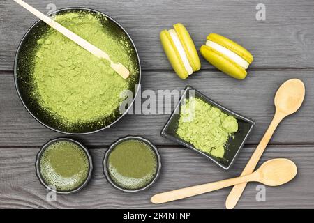 Cuillère graduée dans un bol avec poudre de matcha. Thé vert Matcha et gâteaux macaroni et cuillères en bois sur table. Pose à plat. Arrière-plan en bois sombre Banque D'Images