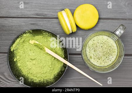 Deux gâteaux de macaroni et une tasse de thé vert matcha. Cuillère graduée dans un bol avec poudre de matcha. Arrière-plan en bois sombre. Banque D'Images