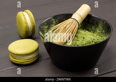 Fouetter le bambou dans un bol avec de la poudre de matcha. Deux gâteaux de macaroni. Arrière-plan en bois sombre Banque D'Images