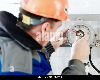Le monteur d'instrumentation vérifie et règle le fonctionnement du manomètre à l'intérieur d'une installation industrielle. Vue arrière Banque D'Images