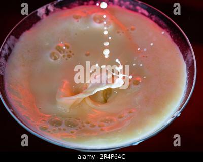 Vue de dessus du cocktail jaune avec vagues et gouttelettes éclaboussant partout dans l'intérieur sombre rougeâtre Banque D'Images
