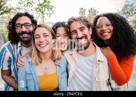 Portrait d'un groupe d'amis en train de rire ensemble et de regarder l'appareil photo. Cinq jeunes gens très chers multiraciaux souriant et s'amusant. Joyeux équipe de démarrage collègues célébrer et se lier ensemble. Photo de haute qualité Banque D'Images