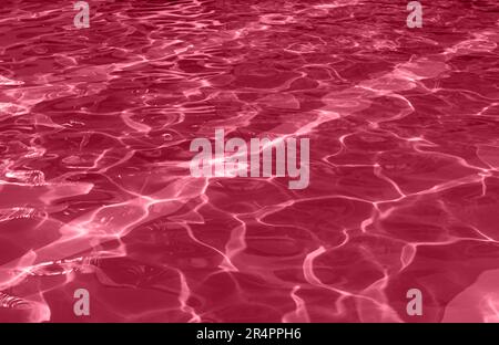 Motif abstrait eau texture caustique arrière-plan avec motif de vague d'ondulation et de réflexion du soleil. Image teintée en couleur de l'année 2023 Viva Magenta Banque D'Images