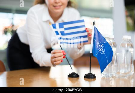 Femme d'affaires qui organise les drapeaux de l'OTAN (OTAN) et de la Grèce pour présentation et négociations Banque D'Images