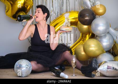 Une femme de race blanche boit du champagne à la bouteille pour fêter son anniversaire de 40 ans lors d'une fête. Banque D'Images