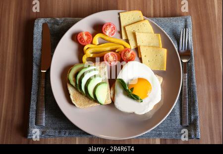 Toasts savoureux avec œufs frits, avocat, fromage et légumes servis sur une table en bois, vue du dessus Banque D'Images