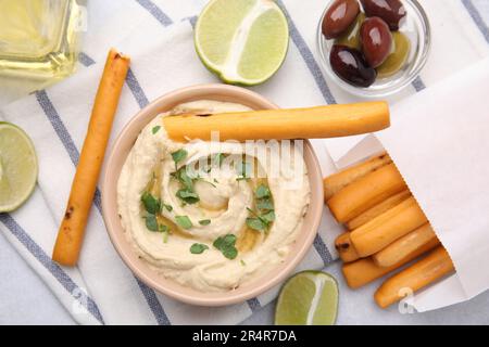 Délicieux houmous avec bâtonnets de graissini, citron vert et olives sur table gris clair, plat Banque D'Images