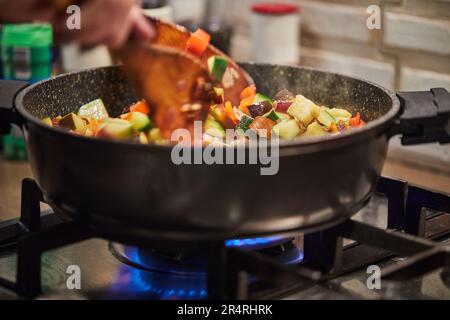 La cuisine française ratatouille salade shchef agite dans une poêle à gaz Banque D'Images