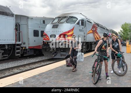 Sur le trottoir dans le chemin de fer Yard deux jeunes femmes se tiennent avec leurs vélos riant, une autre marche avec des sacs dans ses mains le chemin de fer dans le b.g. Banque D'Images