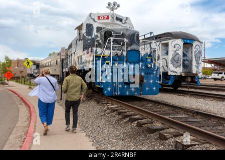 Les touristes, un homme et une femme, marchent vers des voitures de train peintes de couleurs vives, le Sky Railway, garés sur le chemin de fer de Santa Fe Yard à Santa Fe, Nouveau-Mexique, Etats-Unis. Banque D'Images