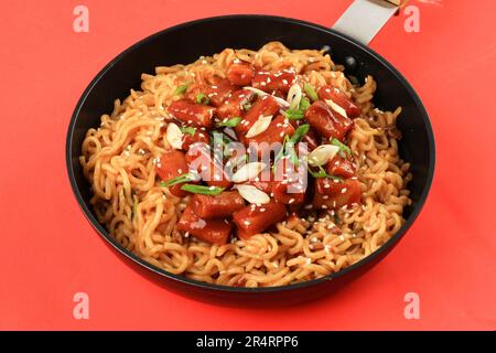 Rapokki ou Rabokki, Ramyeon Tteokbokki avec Korean Ramen Insta Noodle. Gros plan sur le poêle à frire au-dessus de l'arrière-plan de la table rouge Banque D'Images