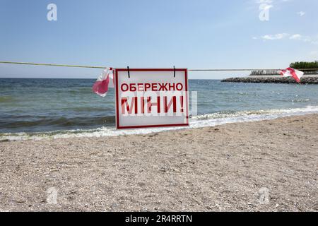 Un panneau rouge vif « danger-mines » en ukrainien est placé sur la plage de sable de la ville à Odessa lors de l'attaque de la Russie contre l'Ukraine. La natation est interdite i Banque D'Images