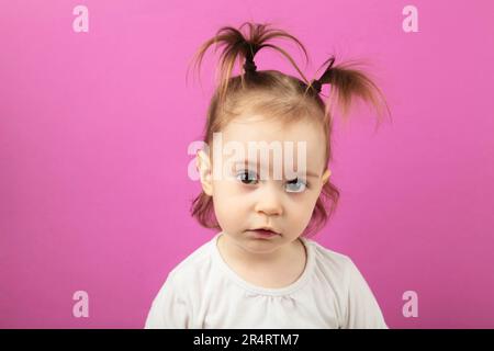 Petite fille caucasienne regardant l'appareil photo avec un sourire adorable, posant sur le rose. Concept d'enfance heureuse. Vue de dessus Banque D'Images