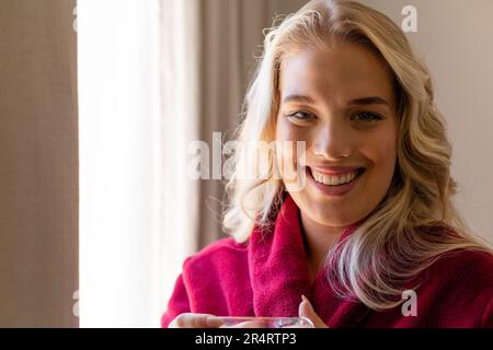 Gros plan portrait de la jeune femme blanche souriante vêtue de peignoir rouge à la maison Banque D'Images