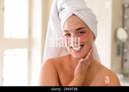 Femme caucasienne souriante de plus grande taille avec une serviette enveloppée sur la tête et des taches rouges sous les yeux Banque D'Images