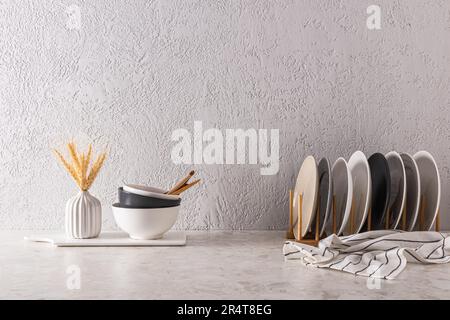 Un ensemble de plaques de céramique sur le sèche-linge de cuisine et des bols sur le plan de travail de la cuisine. Fond de mur texturé gris avec espace pour le texte. minimalisme Banque D'Images