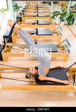 De haut pieds nus femme en activité levant les jambes et faisant un exercice court de colonne vertébrale sur le lit reformeur pendant l'entraînement pilates en studio Banque D'Images